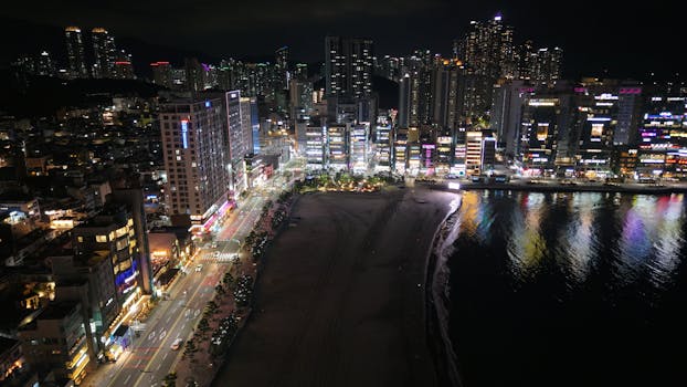 Aerial night view of Busan's illuminated skyline adjacent to the waterfront in South Korea.