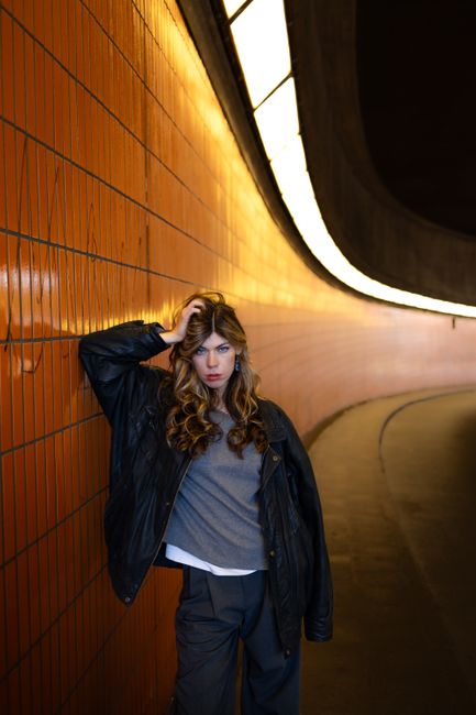 Stylish woman in a leather jacket posing in a dramatic illuminated urban tunnel.