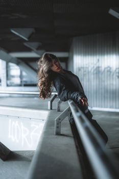 A stylish woman leans dramatically on a railing in an industrial, urban location.