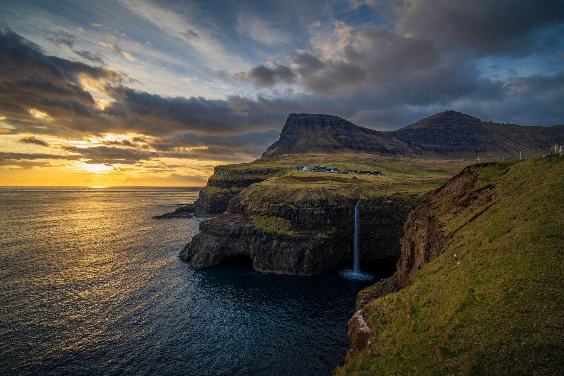 Dramatic sunset over the Mulafossur Waterfall in the Faroe Islands with mossy cliffs.