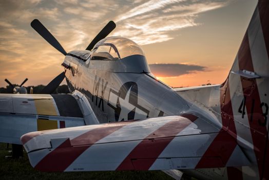A vintage fighter plane, likely a P-51 Mustang, captured at sunset with striking propellers.