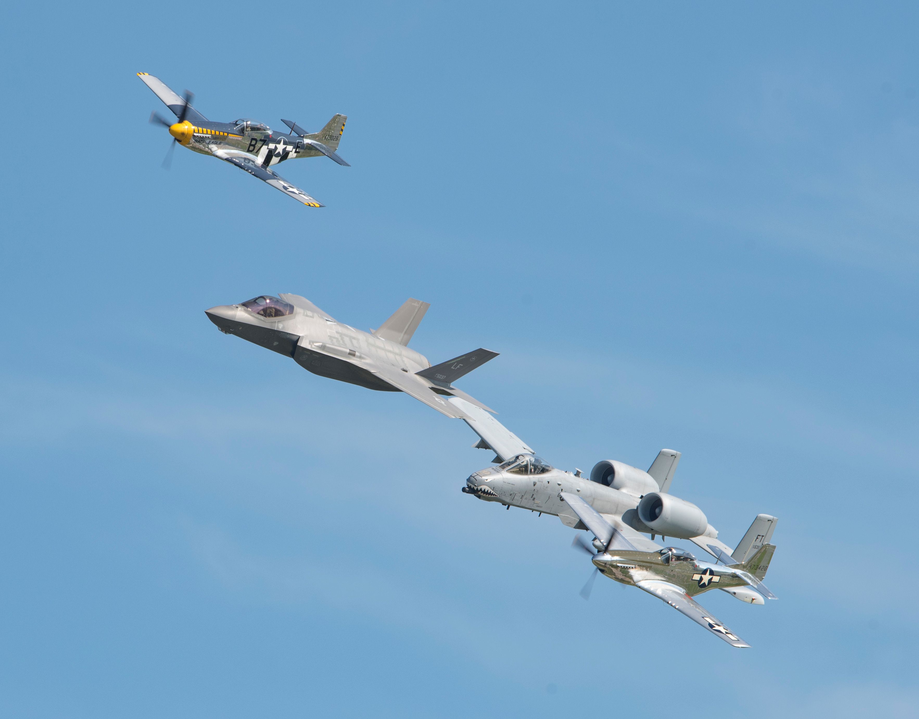 Three different military aircraft flying in formation against a clear blue sky.