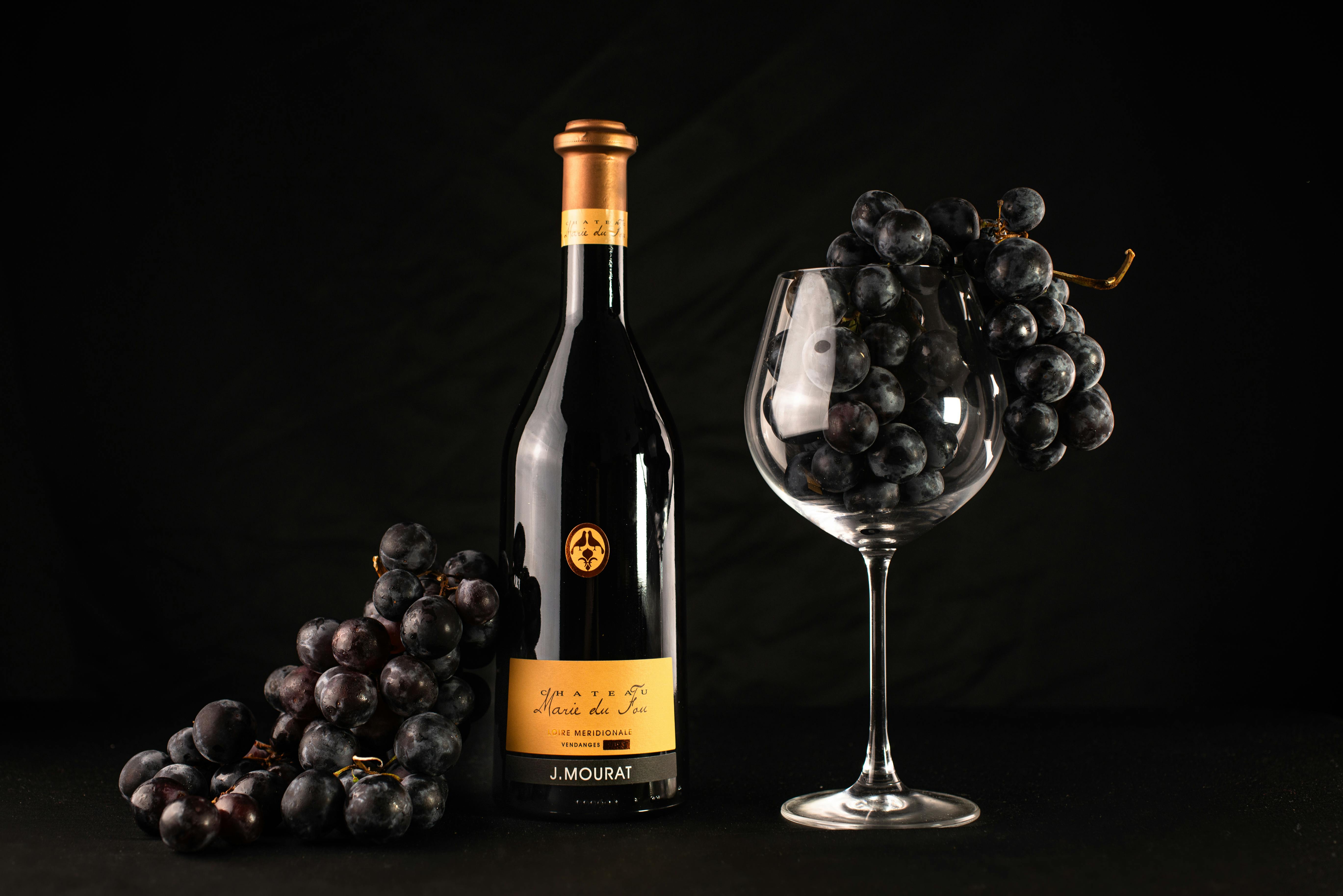 A bottle of red wine with grapes and an empty glass captures elegance and sophistication.