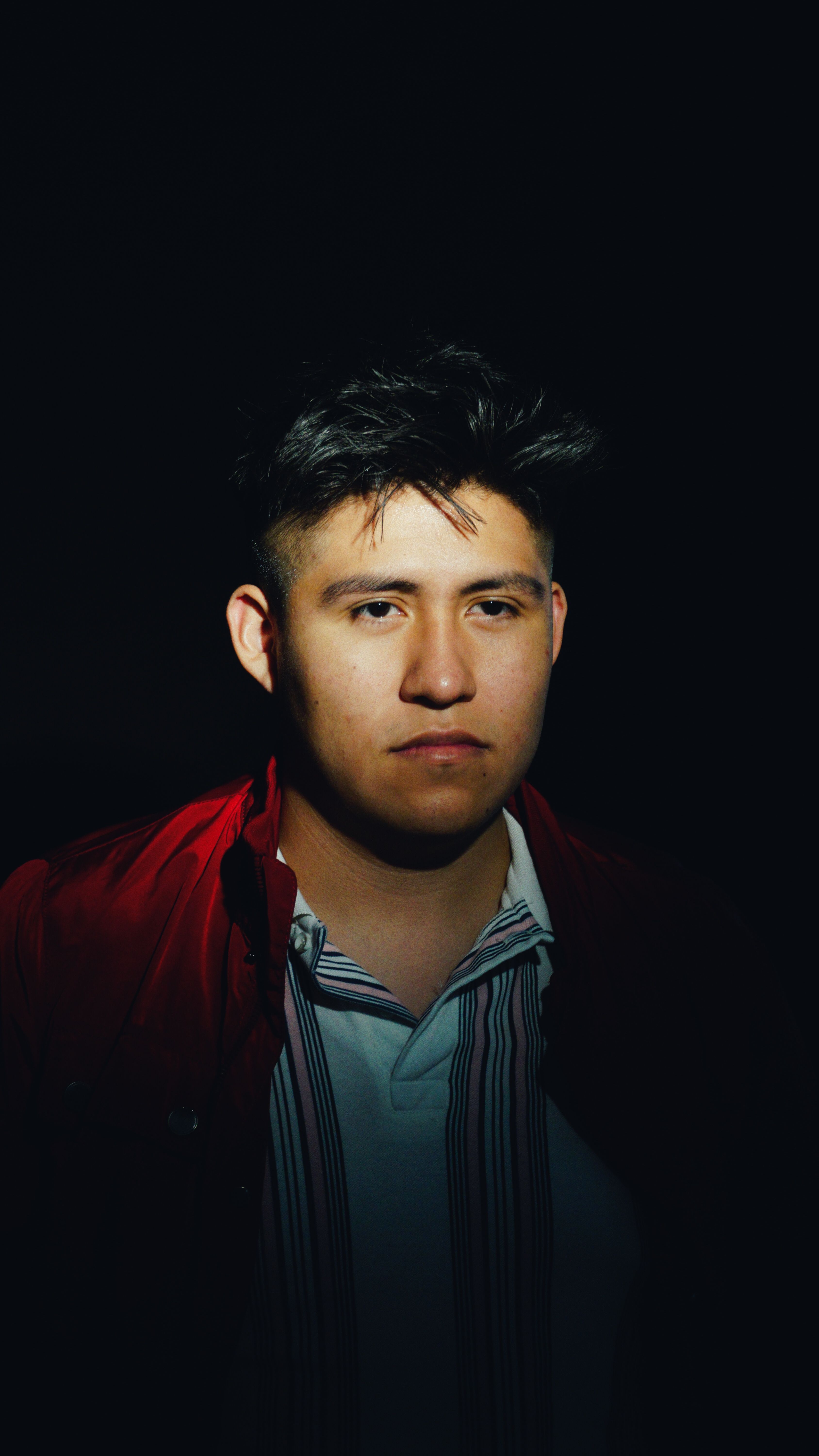 Close-up portrait of a young man with moody lighting, wearing a red shirt.