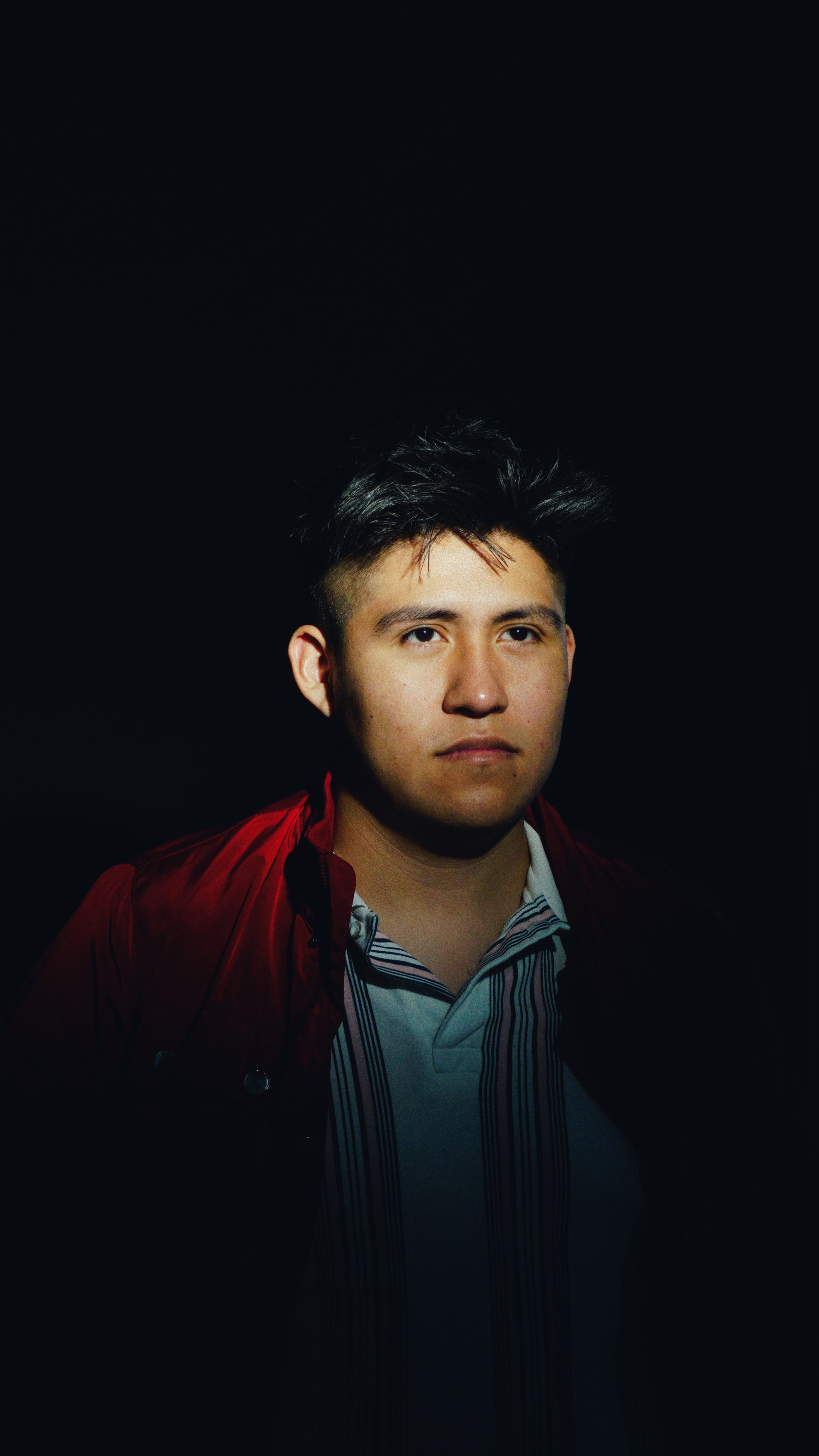 Dramatic portrait of a young adult man with focused light and shadow contrast.