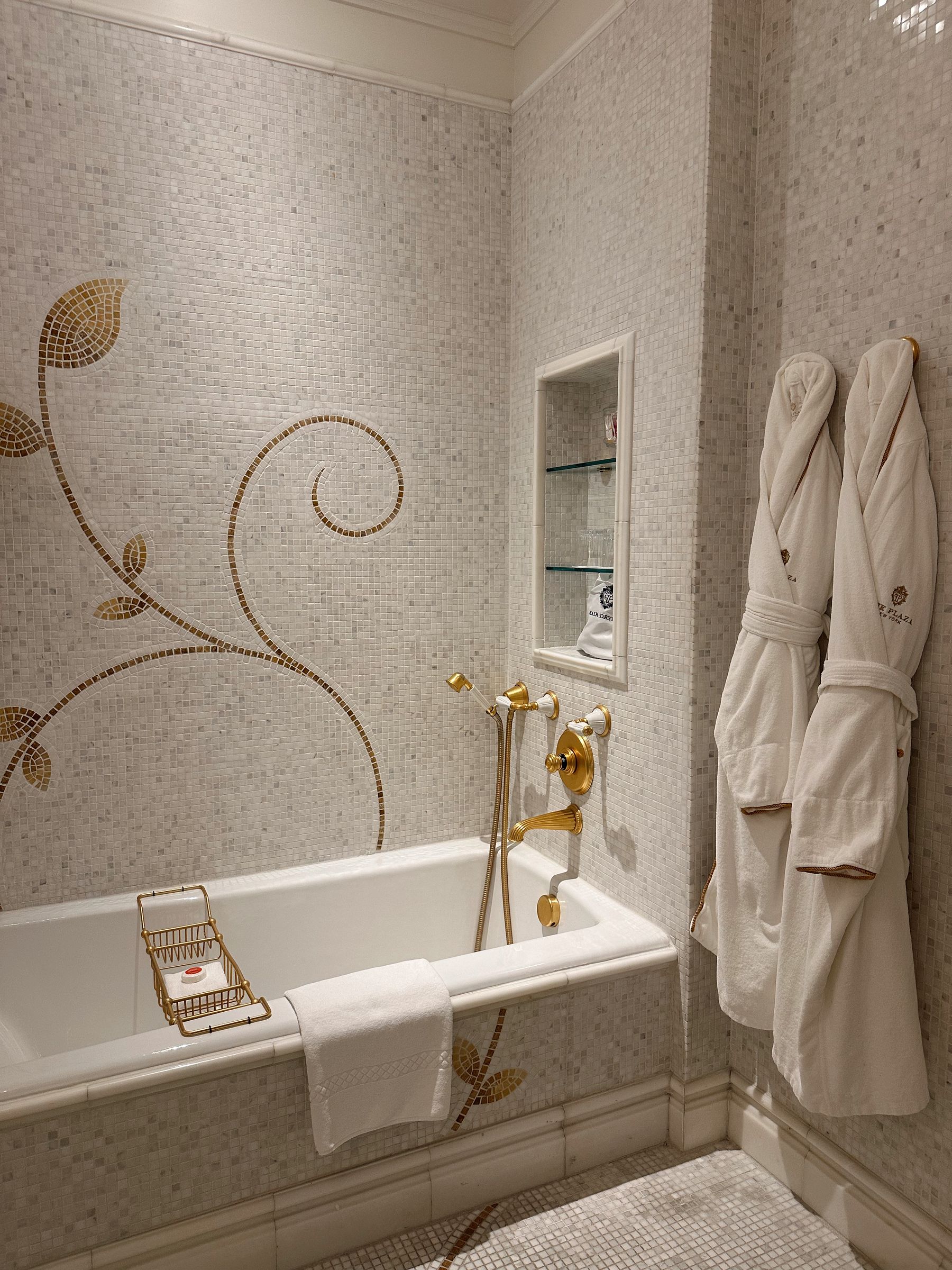 Elegant bathroom with mosaic tile, gold fixtures and white bathrobes