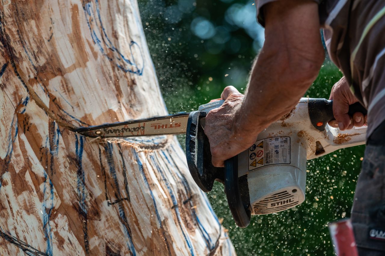 a craftsman using a chainsaw to intricately sculpt a wooden statue out