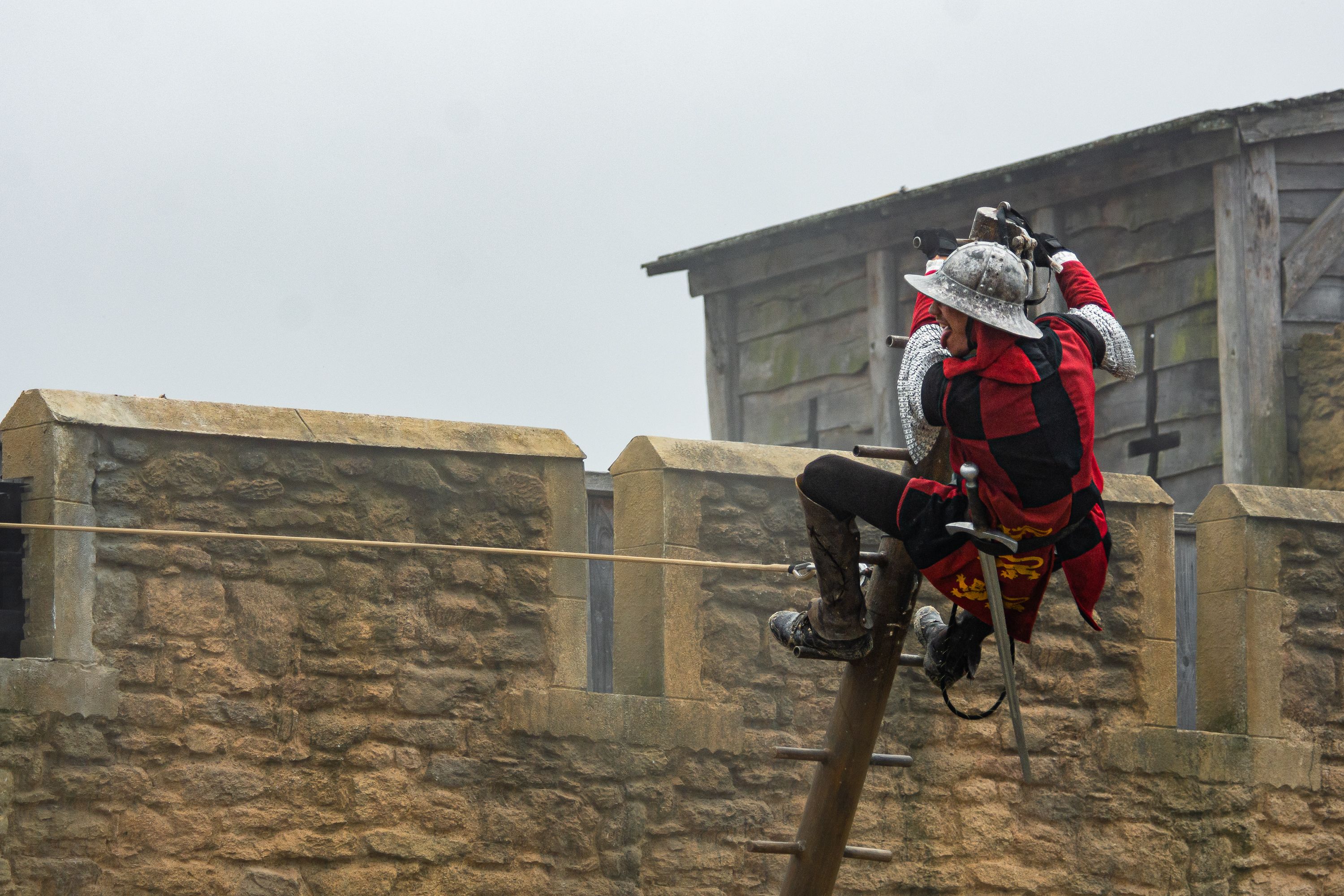 A medieval knight in armor ziplining across a castle wall in an outdoor setting.