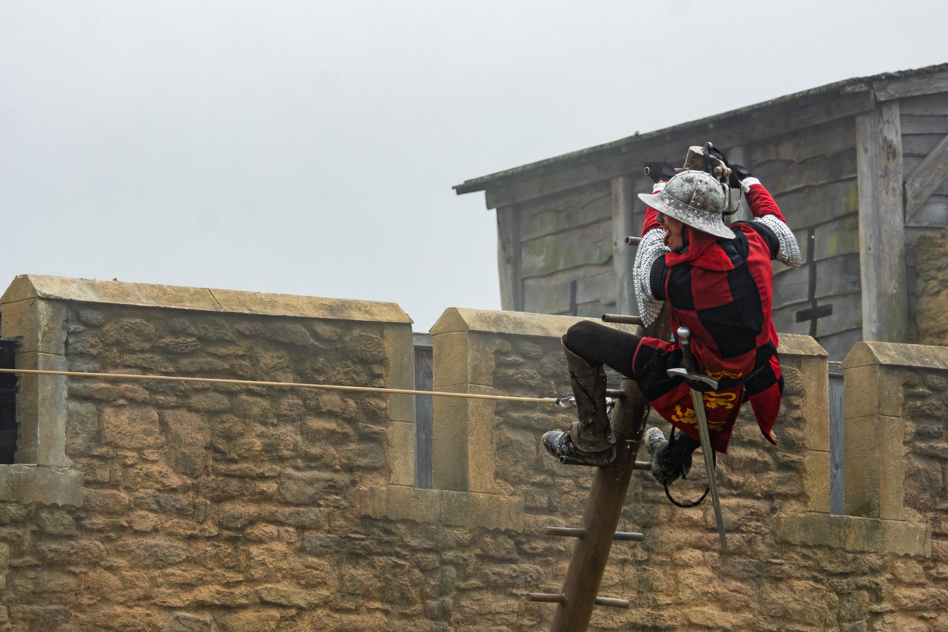 A medieval knight in armor ziplining across a castle wall in an outdoor setting.