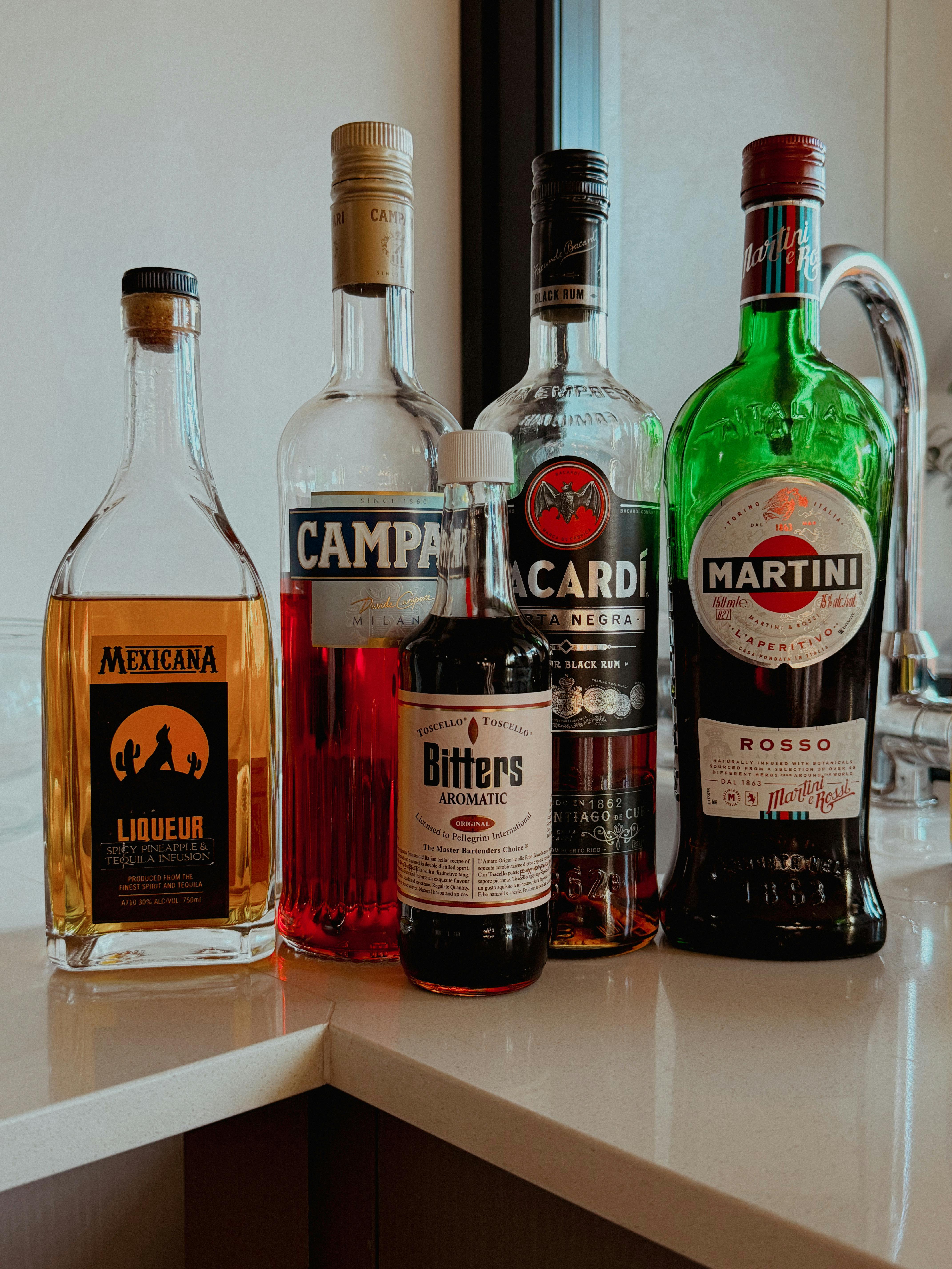 A selection of liquor bottles including Campari and Martini displayed on a kitchen counter.