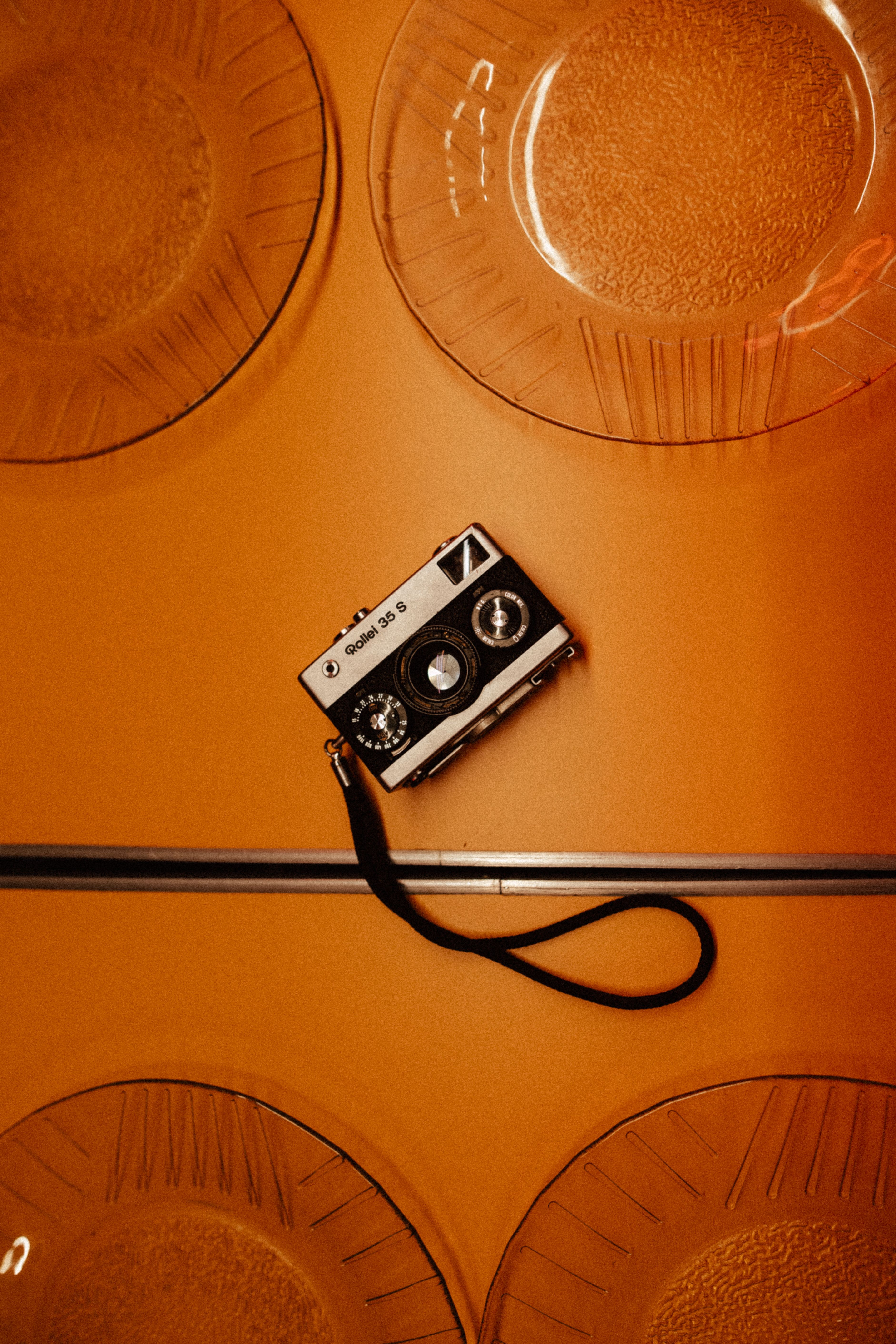 Retro analog camera with a strap on a vibrant orange surface surrounded by clear textured plates.