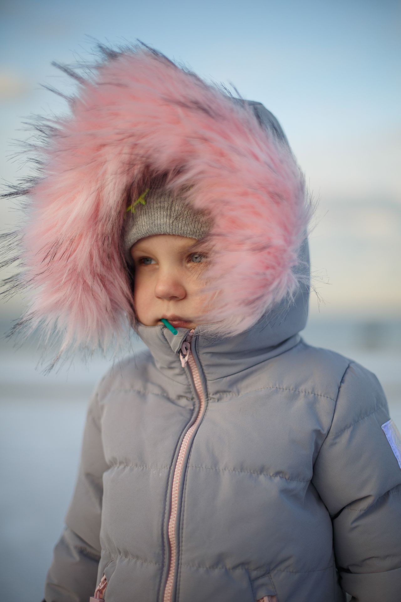 Girl in a gray puffer coat with a pink faux-fur-trimmed hood in the snow