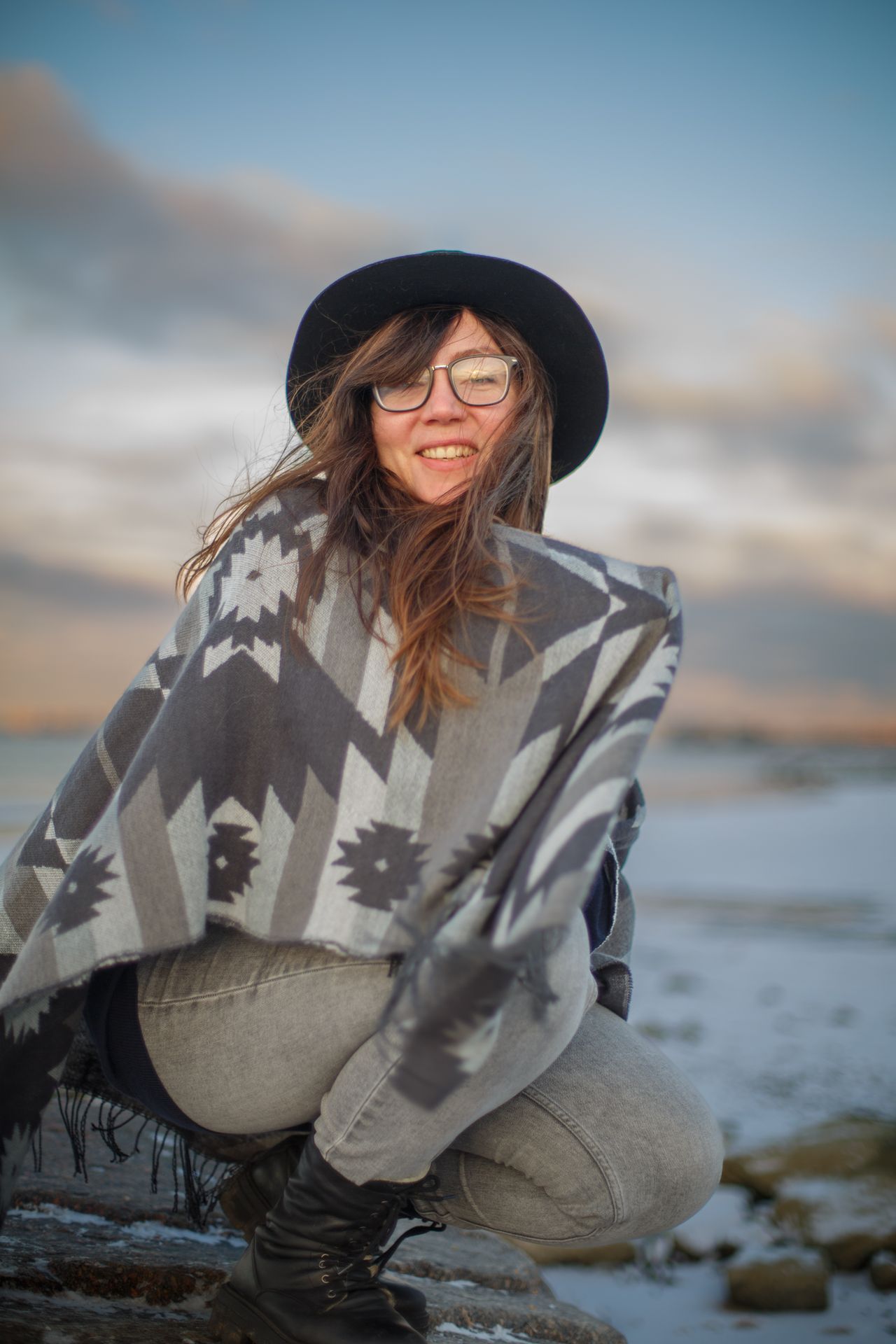 Woman in a gray patterned poncho wrap and hat on a snowy beach