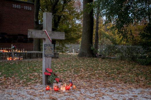 A peaceful cemetery scene with a cross, memorial candles, and autumn leaves.