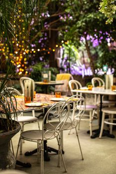 Cozy outdoor café with vintage seating amidst greenery and fairy lights, perfect for a relaxing evening.