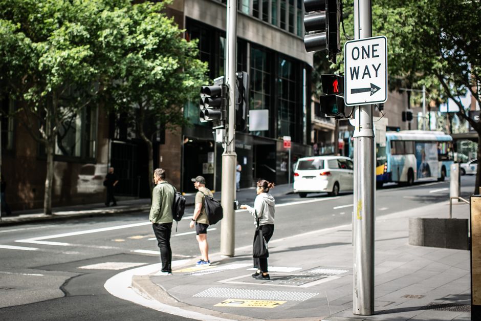 People waiting at a crosswalk on a sunny day in Alexandria, New South Wales with prominent one-way signage.