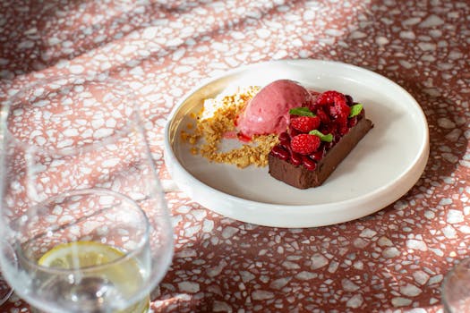 Elegant dessert of chocolate cake, raspberries, and sorbet on a patterned table.