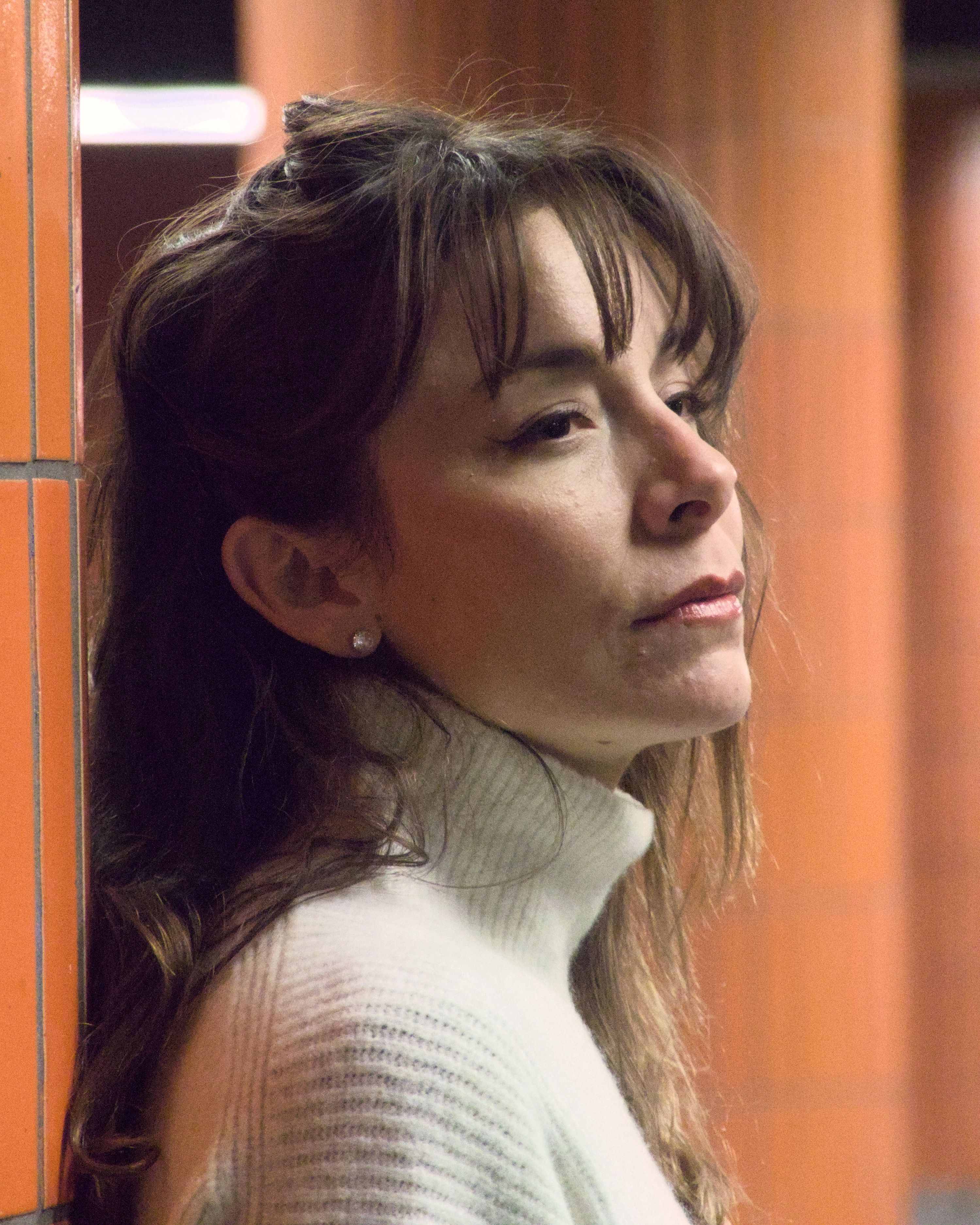 A woman leans against a tiled wall in a Berlin subway station, lost in thought.