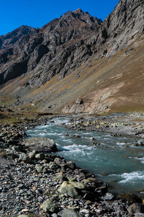 Free Pristine mountain river coursing through rugged, rocky landscape under clear blue sky. Stock Photo