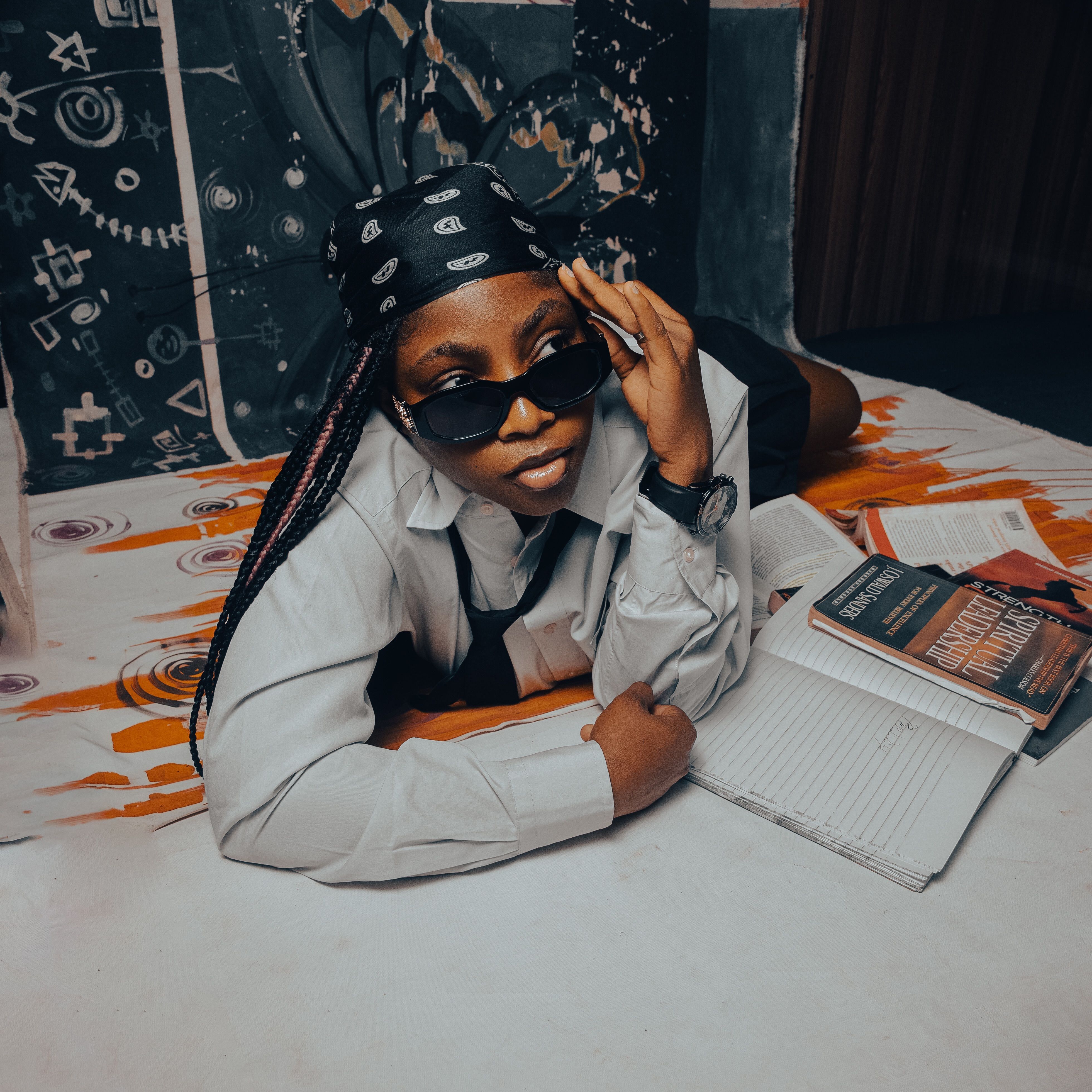 A cool student wearing sunglasses and bandana poses with study materials in an artistic setting.