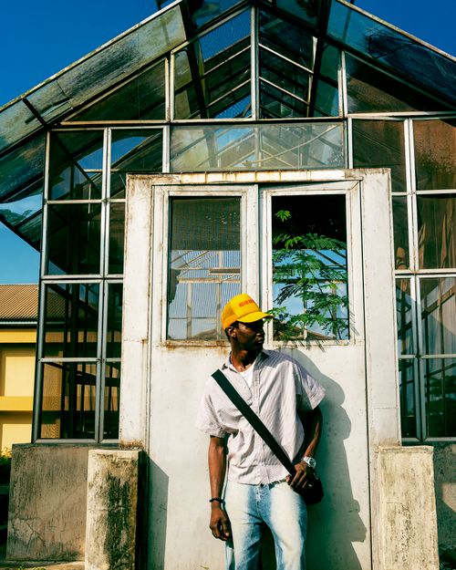 Free Young man with a yellow cap poses in front of a glass greenhouse on a sunny day. Stock Photo