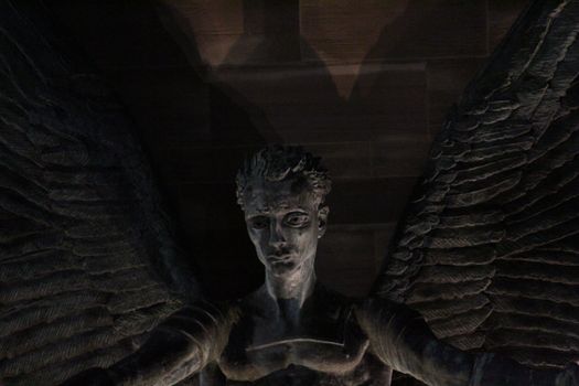 A dark and dramatic bronze angel statue with detailed wings in low light.