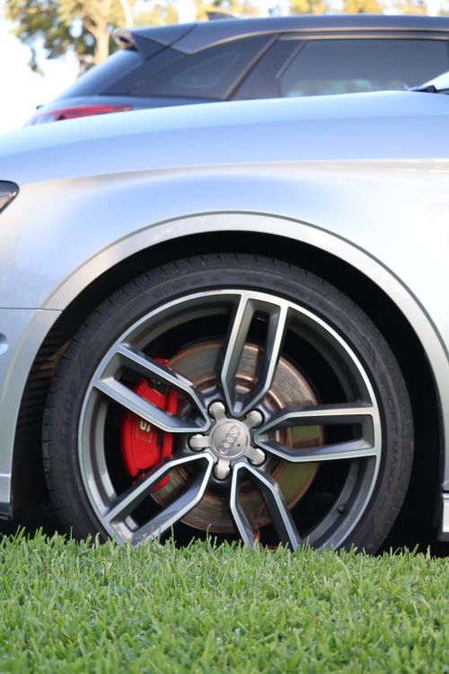 Free Detailed view of a luxury car wheel with red brake calipers on grass. Stock Photo