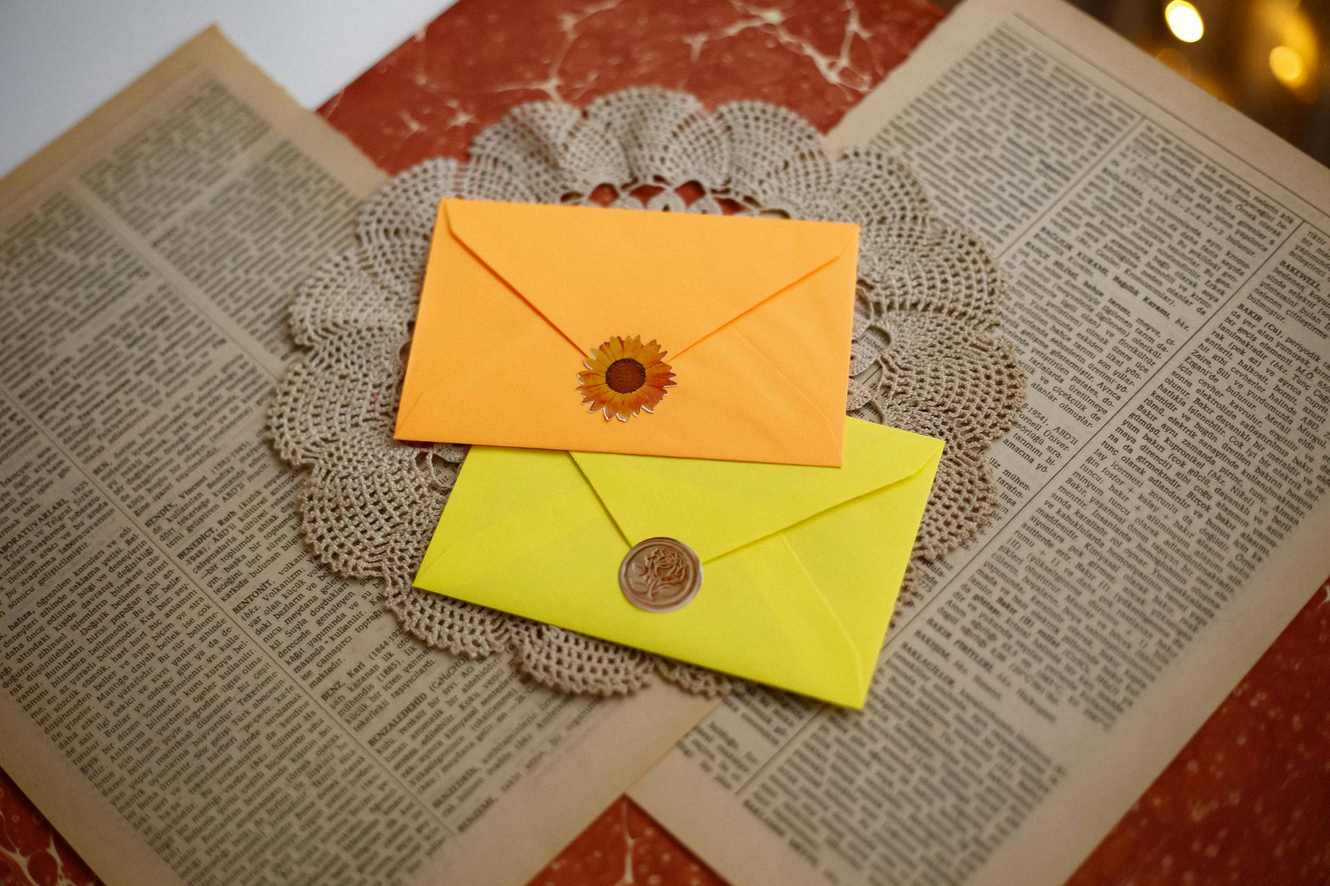 Bright orange and yellow envelopes on vintage paper with crochet doily decor.
