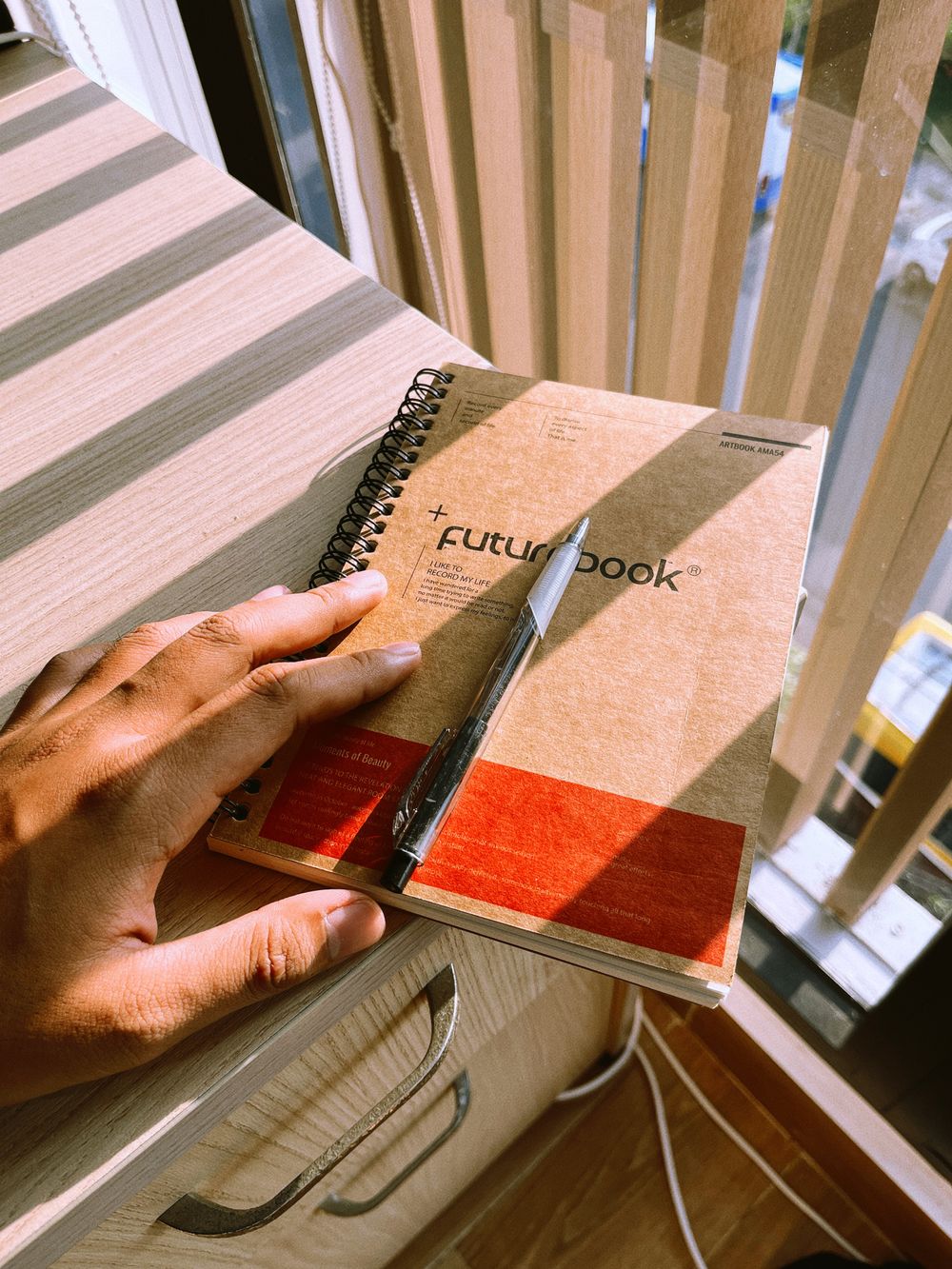 Hand holding a small notebook with a pen, ready to capture a passing thought