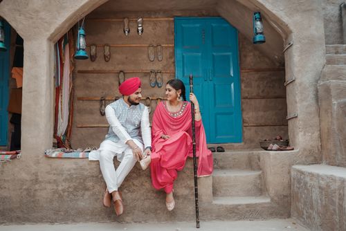 Free A smiling couple in traditional Punjabi attire sitting together in a rustic village setting. Stock Photo