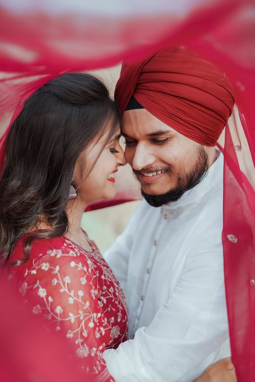 Free A loving couple in traditional attire sharing a tender moment under a red veil. Stock Photo