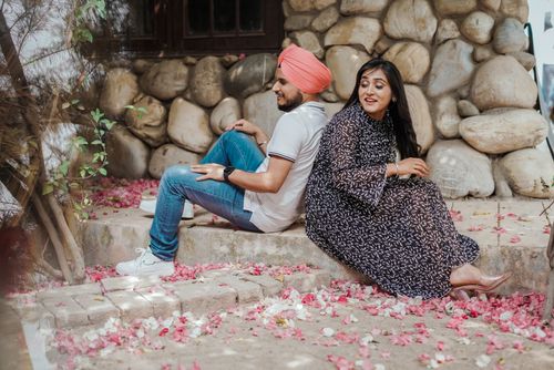 Free A joyful couple seated back-to-back on stone steps amidst fallen pink petals. Stock Photo