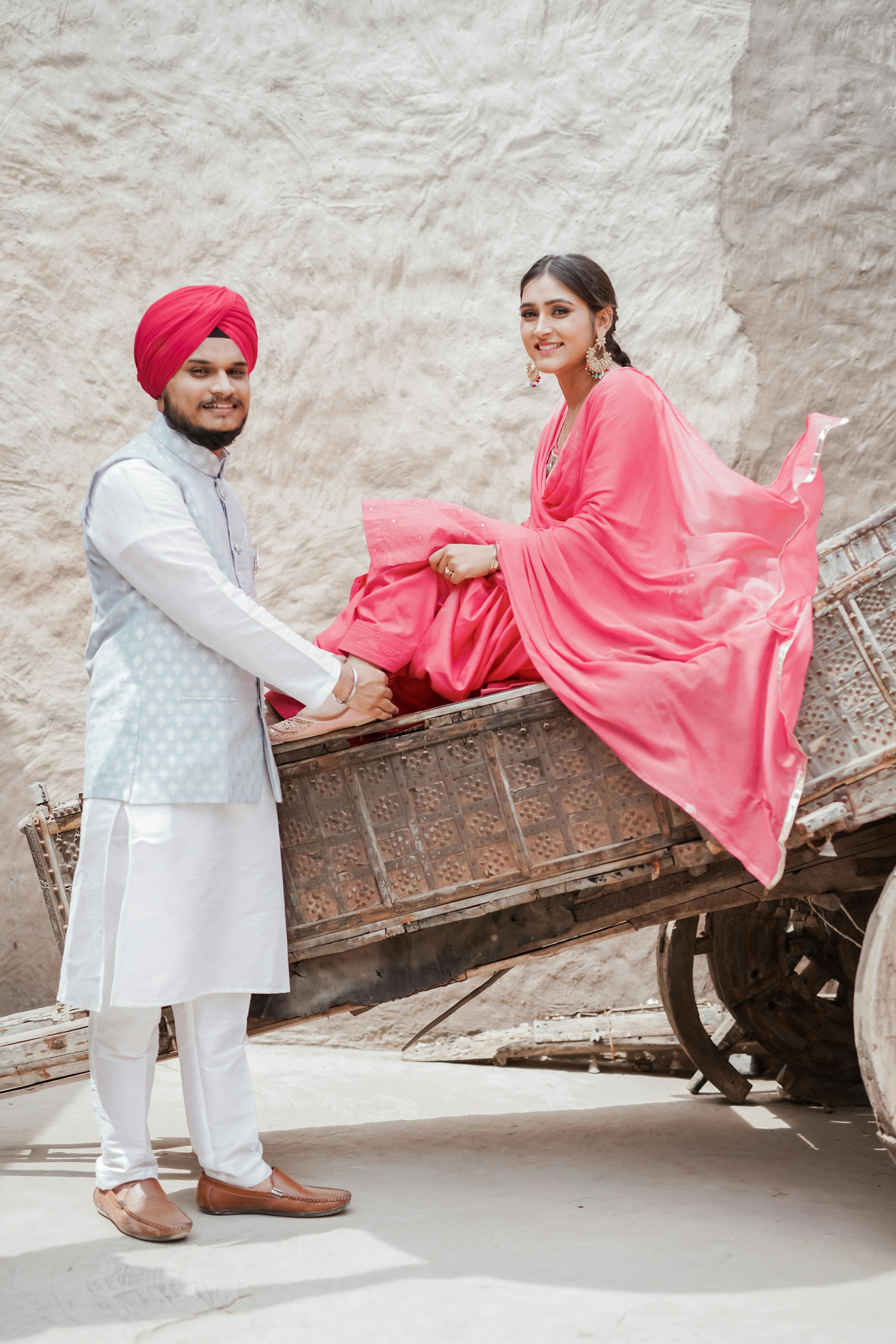Smiling Indian couple in traditional dress outdoors, with woman sitting on a wooden cart.