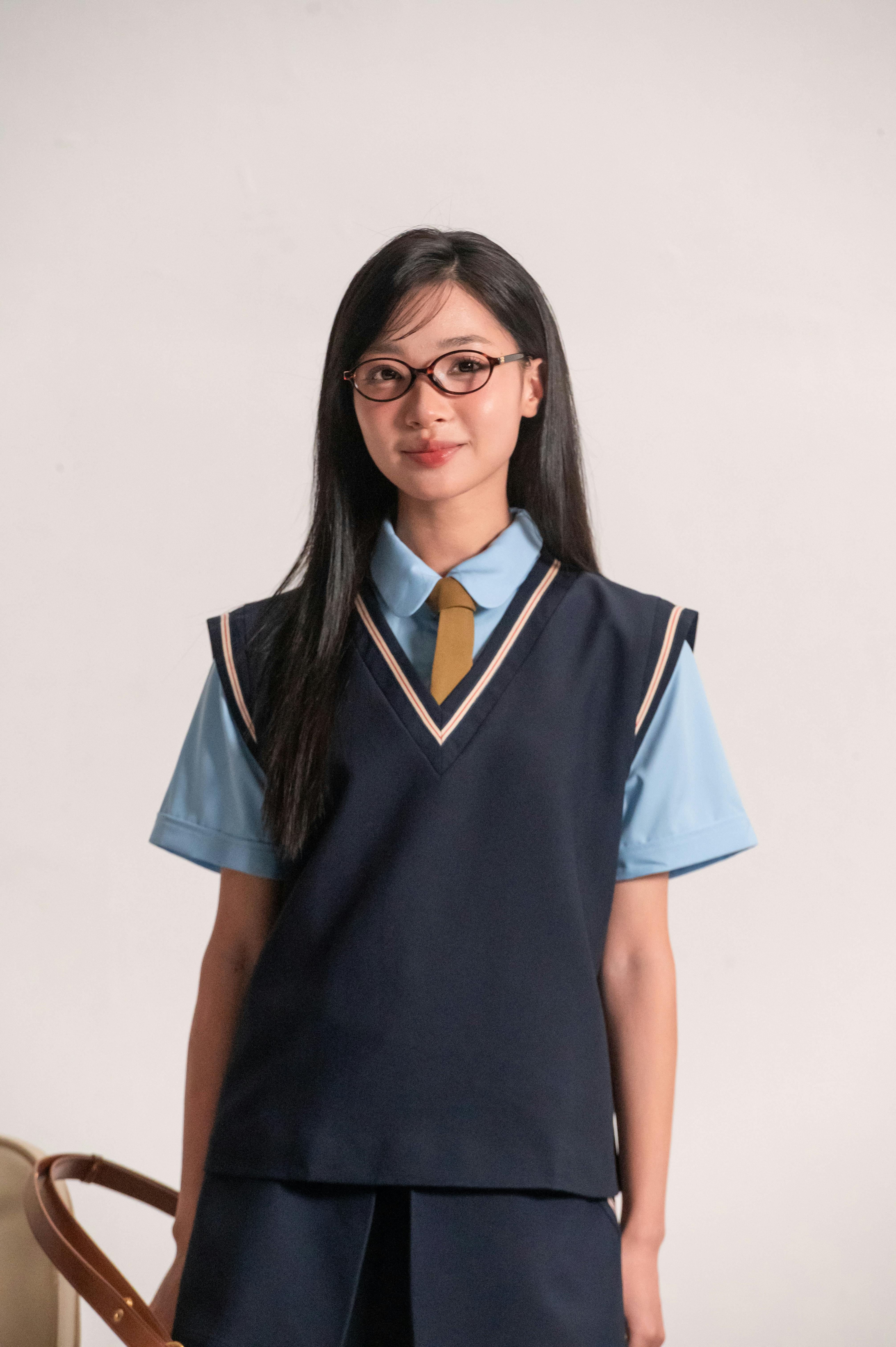 Young woman in a school uniform posing indoors against a neutral background.
