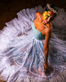 Elegant dancer in a white dress with floral face art viewed from above.