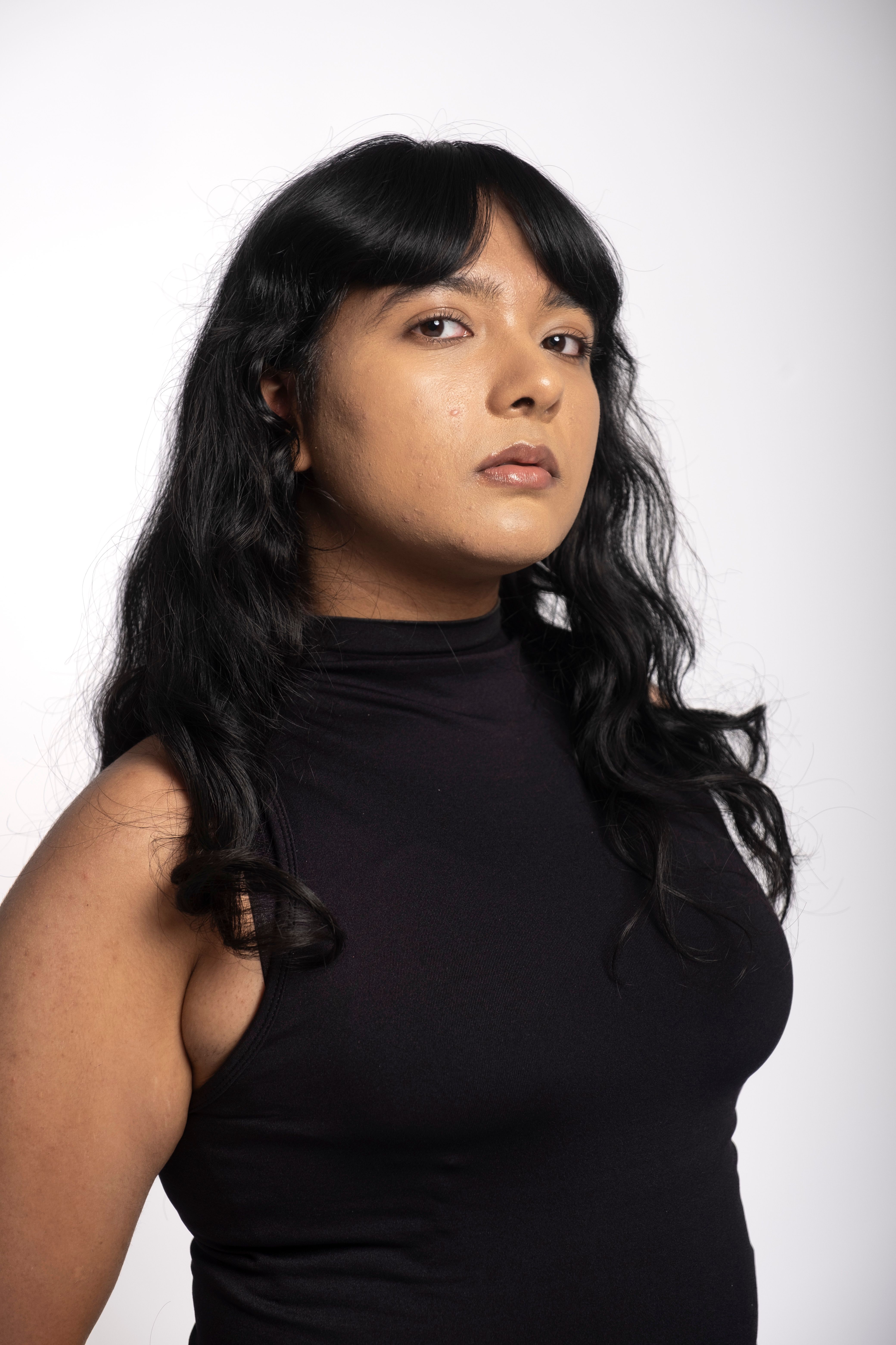 Portrait of a confident woman with long dark hair, looking self-assured in a black sleeveless top.
