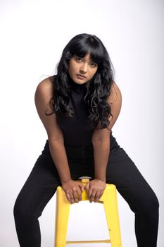 Confident woman poses on a vibrant yellow stool against a white backdrop.