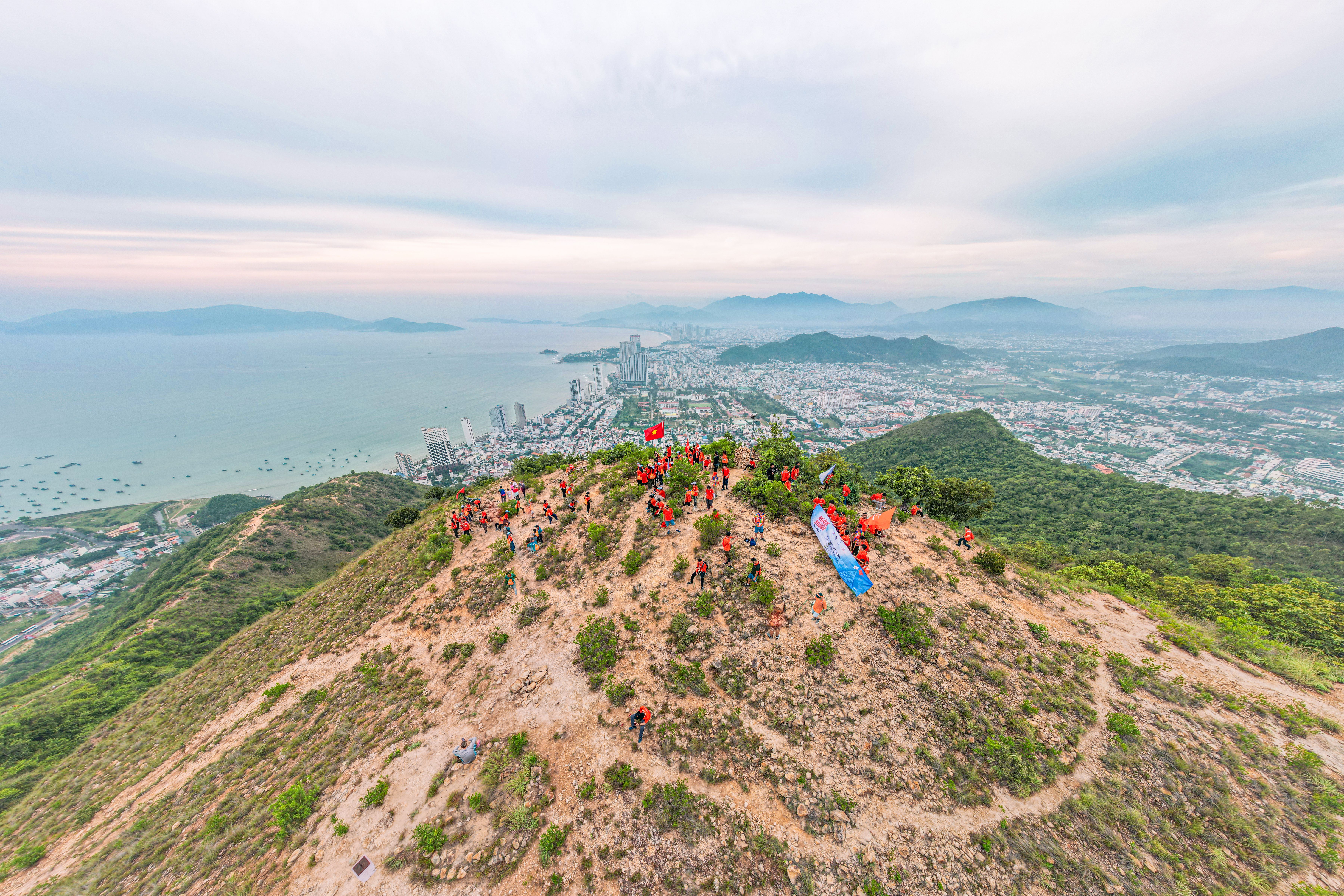 A vibrant aerial view of a large group on a coastal mountain with a city backdrop.