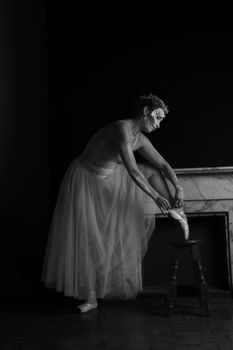 A graceful ballerina adjusts her pointe shoes in a timeless black and white scene.