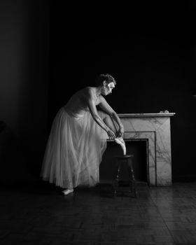 Black and white photo of a ballerina adjusting her pointe shoe, exuding grace and elegance.