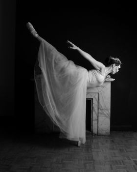 Elegant black and white photo of a ballerina performing an arabesque pose indoors.
