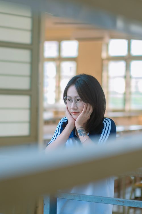 Free A young woman in a casual outfit gazes thoughtfully in a bright, sunlit classroom. Stock Photo