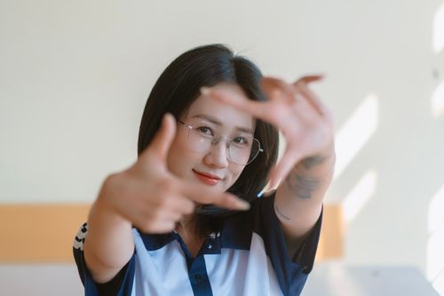 Free A young woman smiles as she frames her face with her hands in a sunlit room. Stock Photo