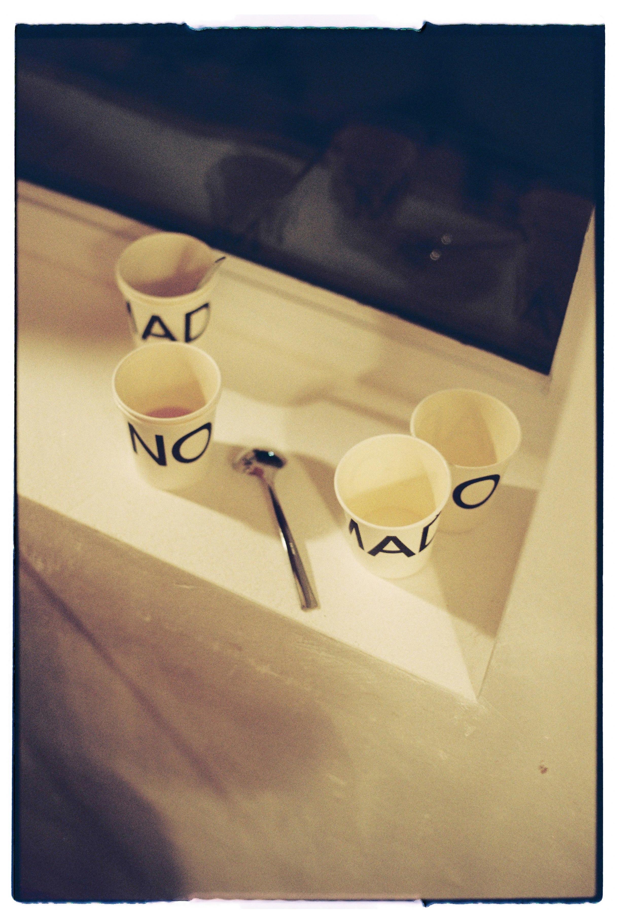 A creative still life with labeled paper cups and spoon on a table.