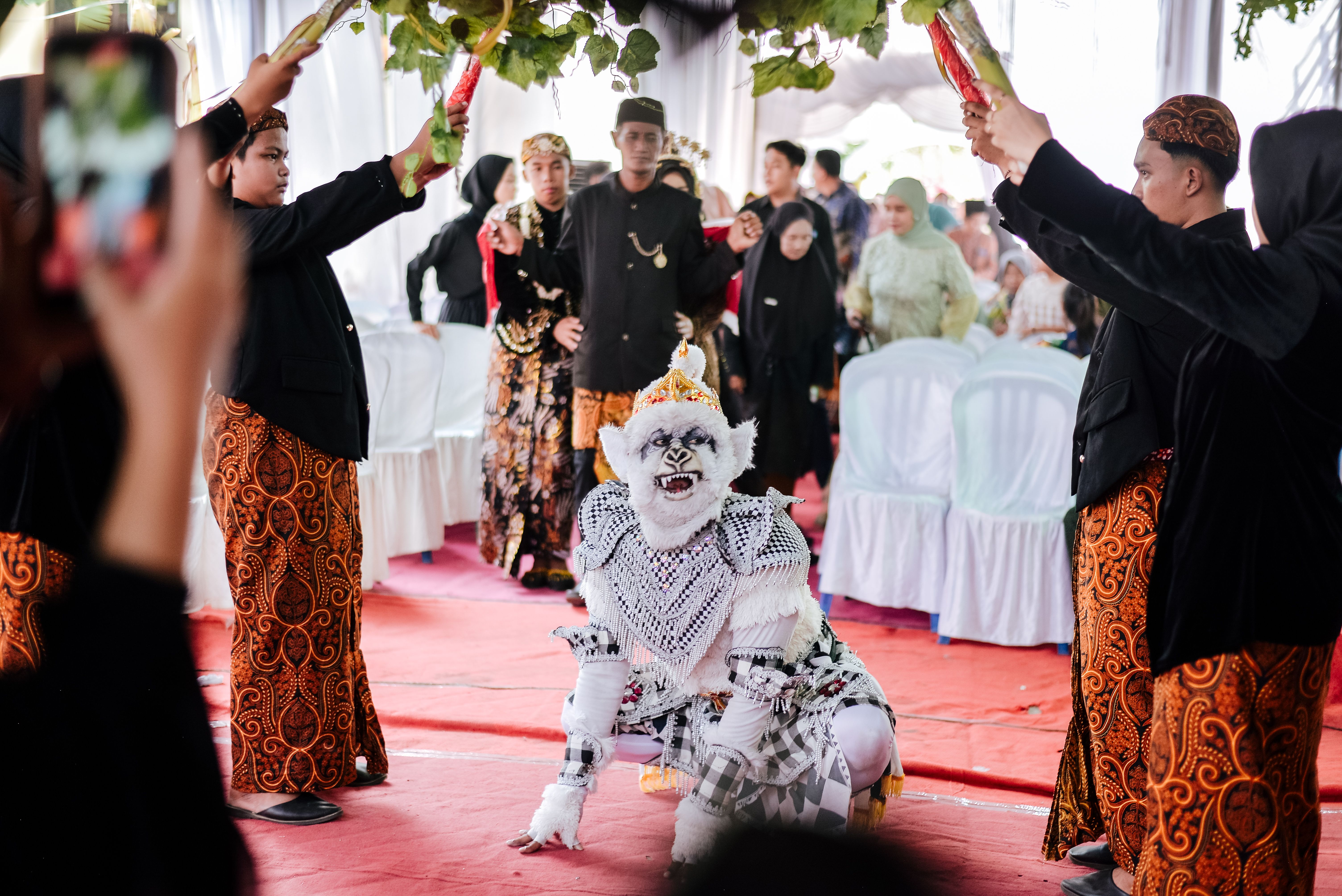 A vibrant scene from a Javanese wedding featuring a traditional masked dancer in ornate attire.