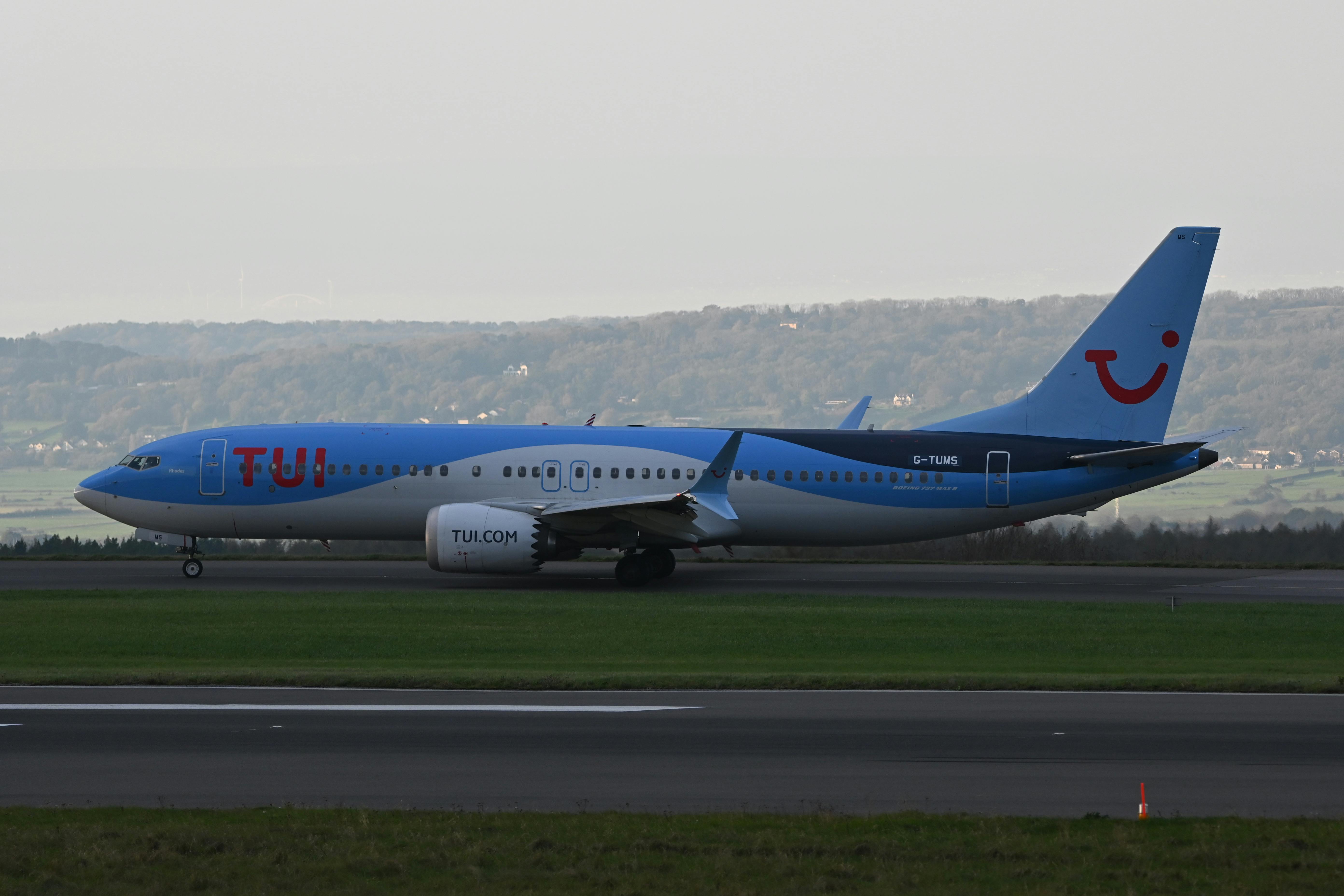 TUI airplane taxiing on a runway with a scenic landscape in the background.
