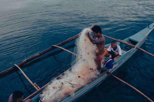 Free Fishermen handling nets on a small boat in tranquil blue waters during twilight. Stock Photo
