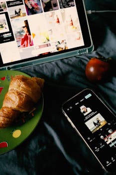Cozy flat lay with croissant, smartphone, and tablet on a bedspread.
