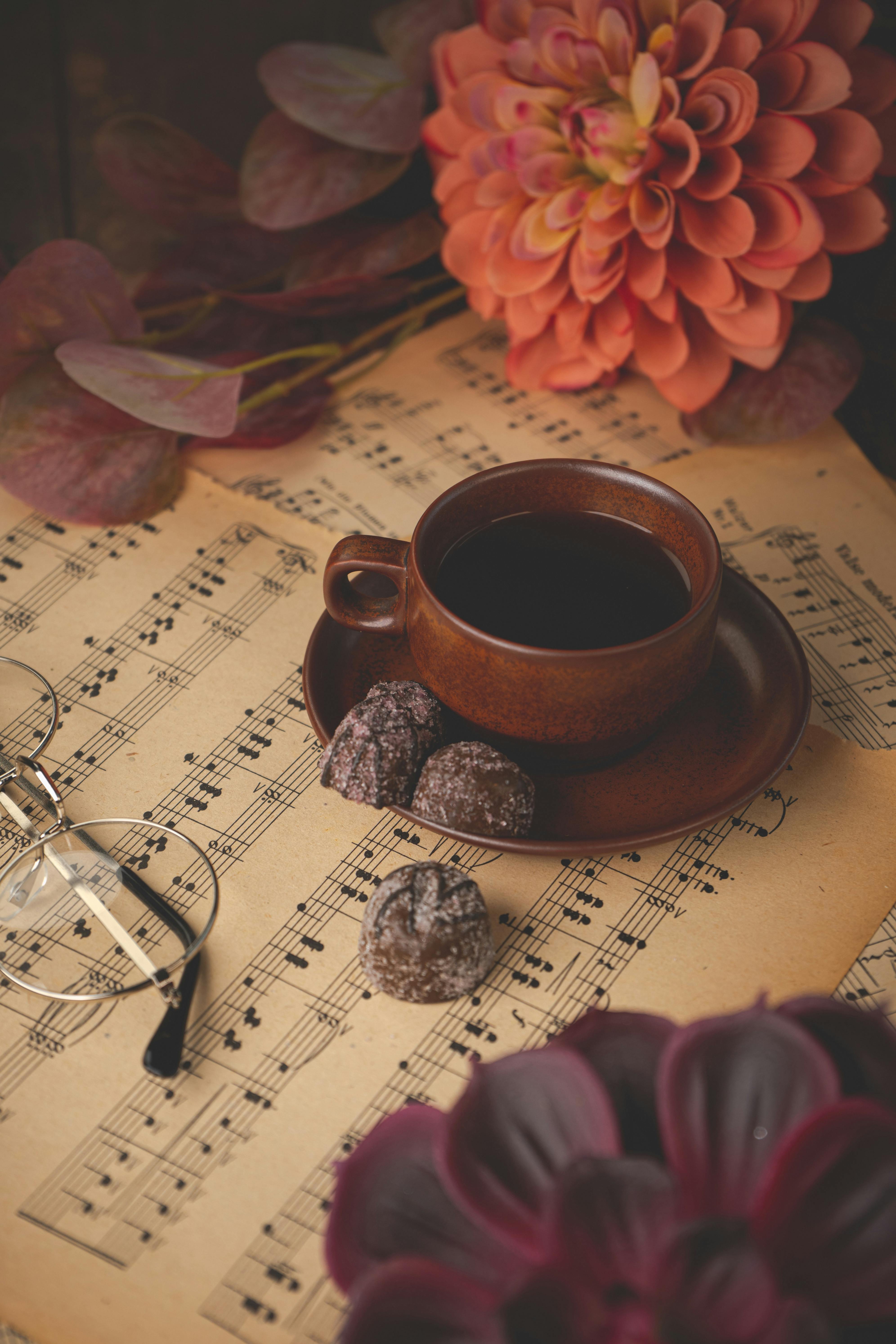 Warm autumn coffee setup with chocolates on vintage sheet music, surrounded by flowers.