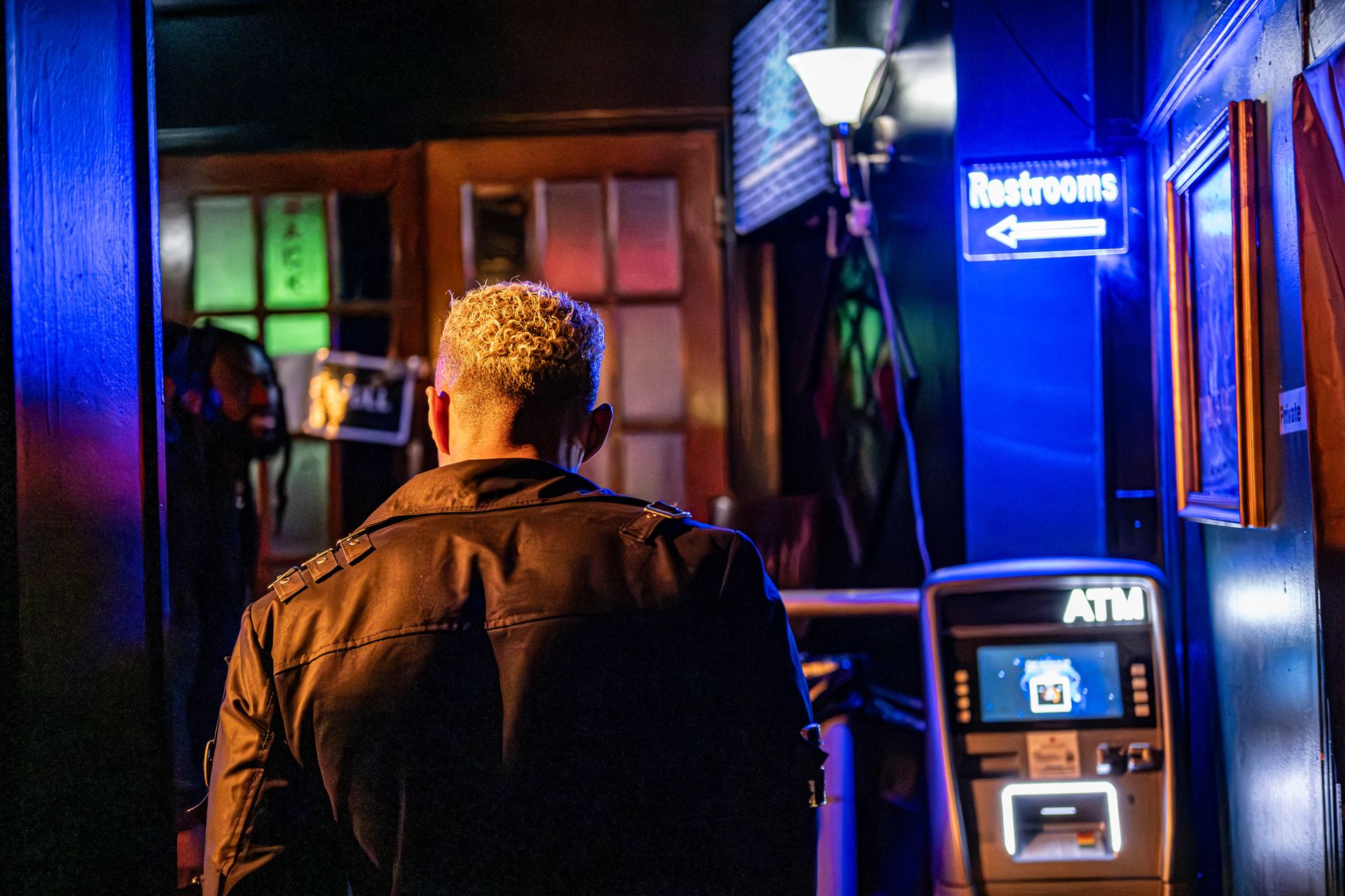 Back view of a person in a bar with vibrant neon lights and an ATM, Toronto.